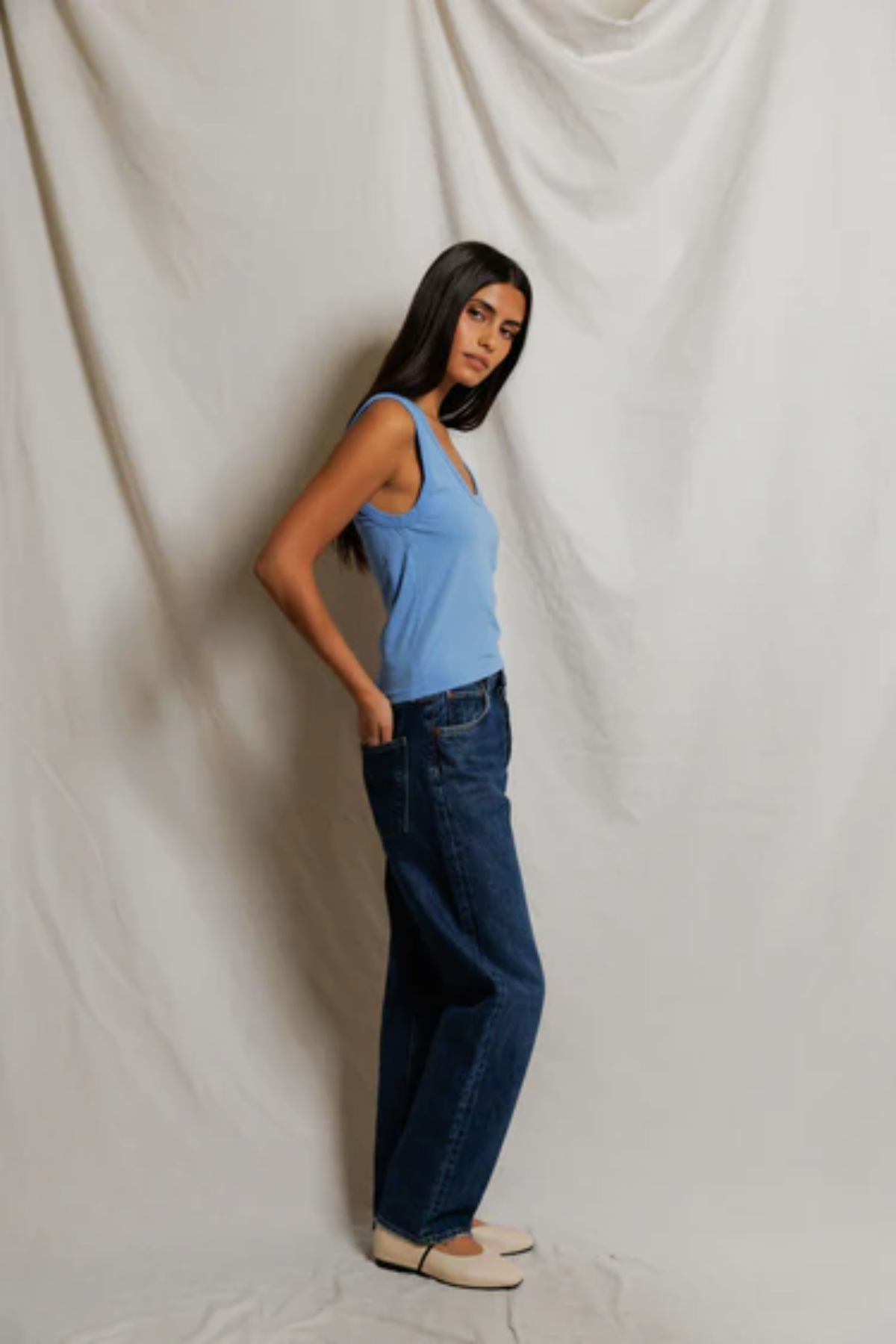Woman wearing a blue top and dark jeans against a plain white background