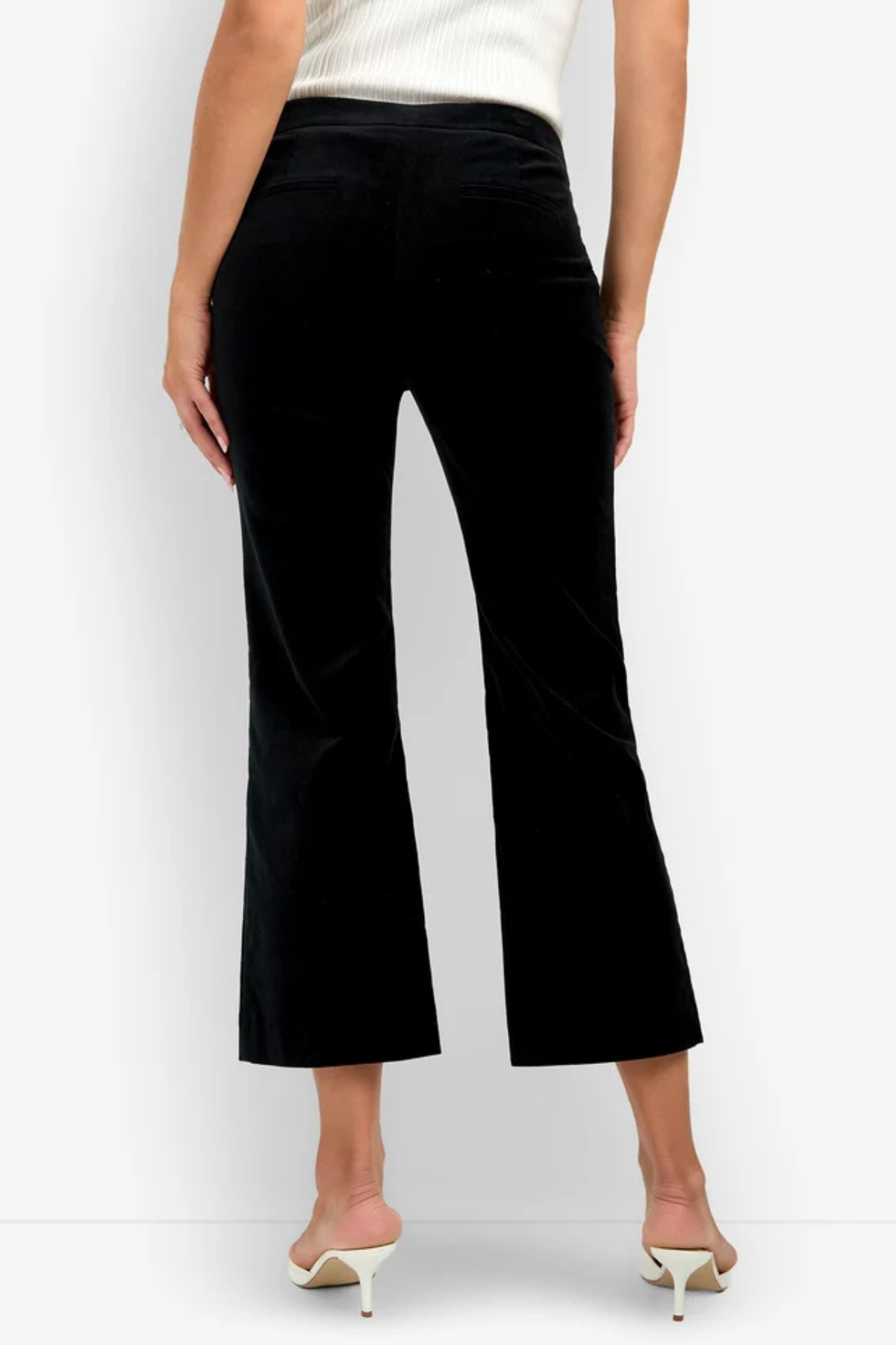 Black velvet cropped flare pants shown on a model from the back, paired with a white ribbed top and white heeled sandals against a white studio background.