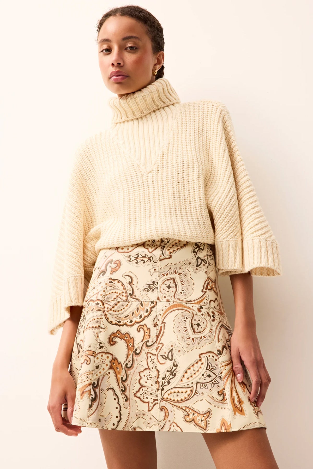 Woman wearing a cream sweater and patterned skirt against a white background