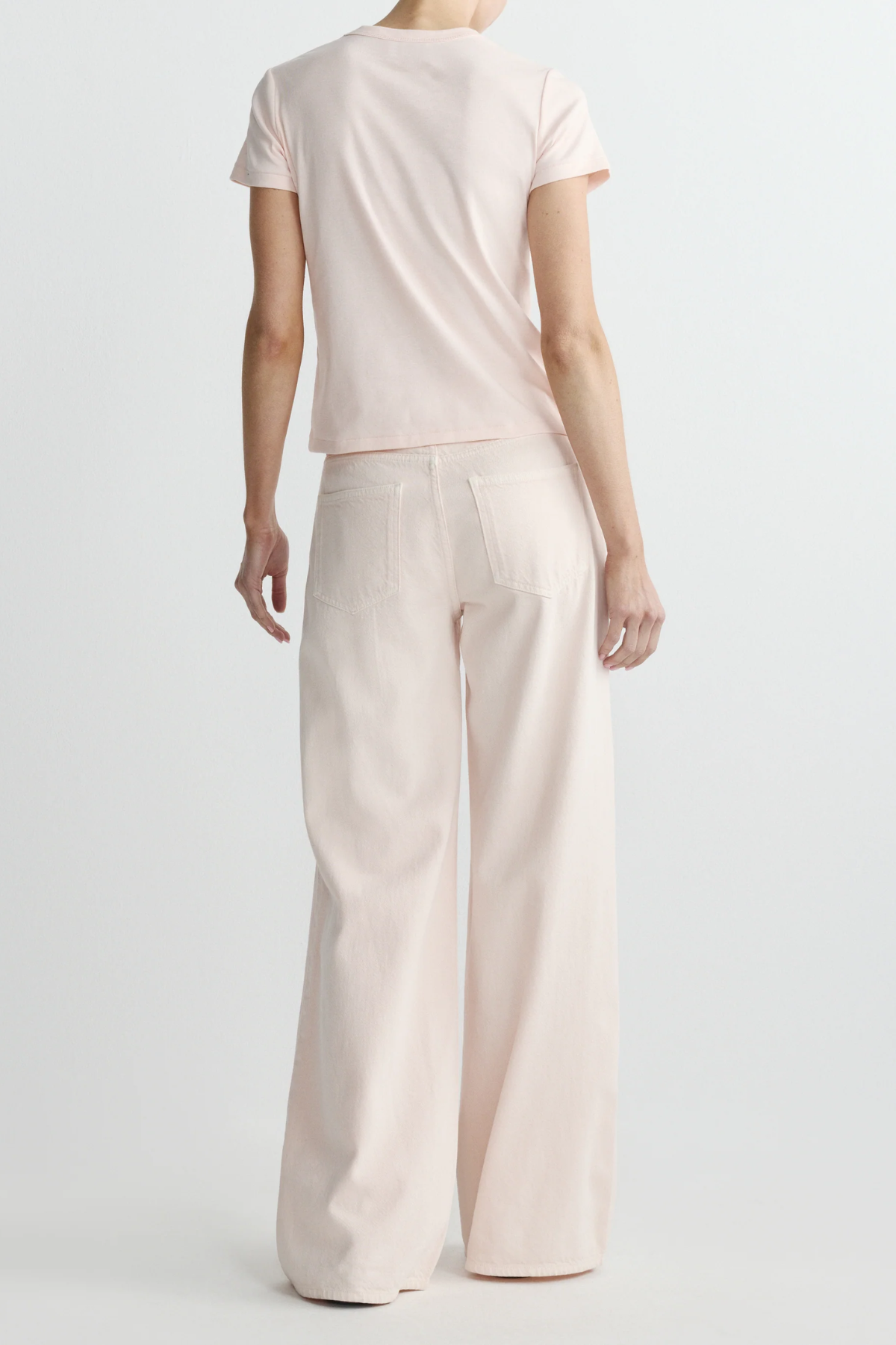 Person wearing a light pink top and wide-leg pants on a white background
