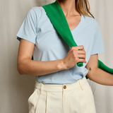 Woman wearing a light blue shirt with a green strap over her shoulder against a neutral background