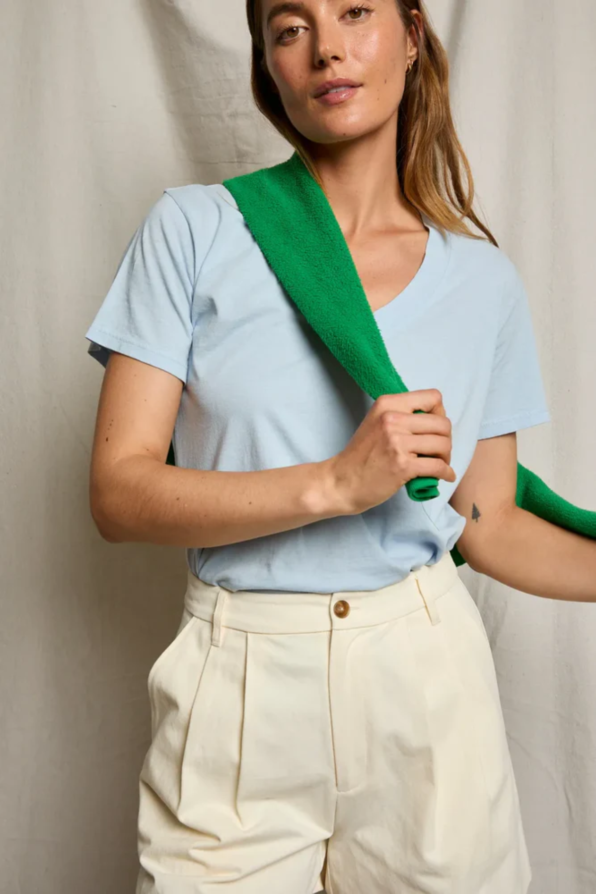 Woman wearing a light blue shirt with a green strap over her shoulder against a neutral background