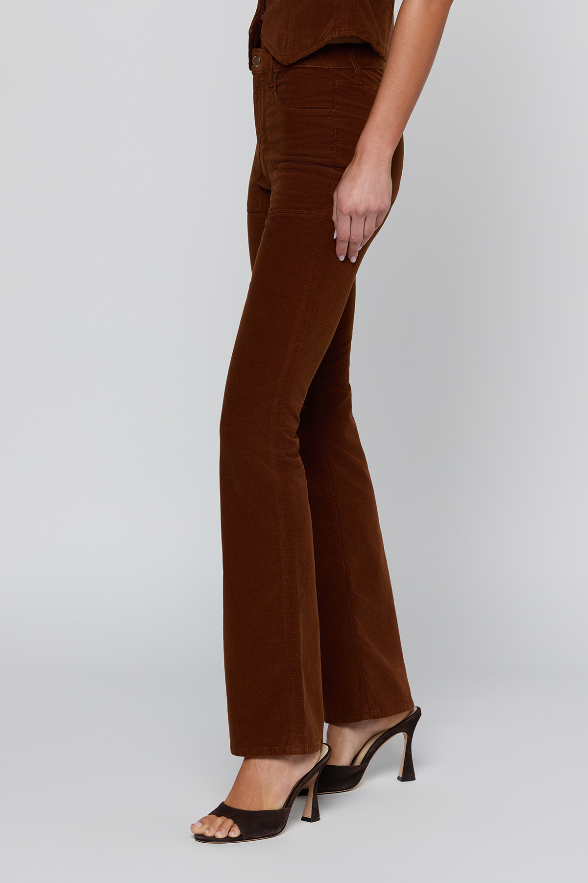 A model wearing brown corduroy flare pants and dark brown heeled sandals, shown from the waist down against a light gray studio background.