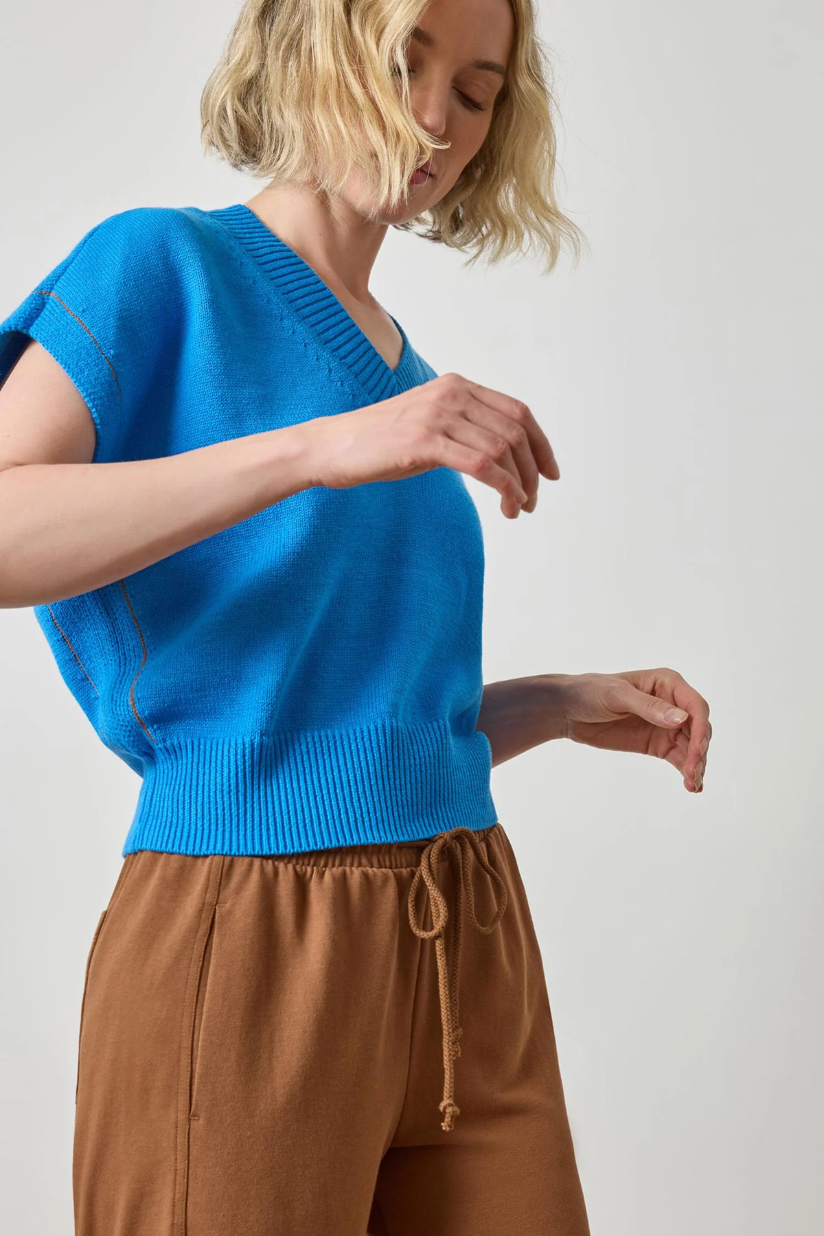 Woman wearing a blue sweater and brown pants on a plain background