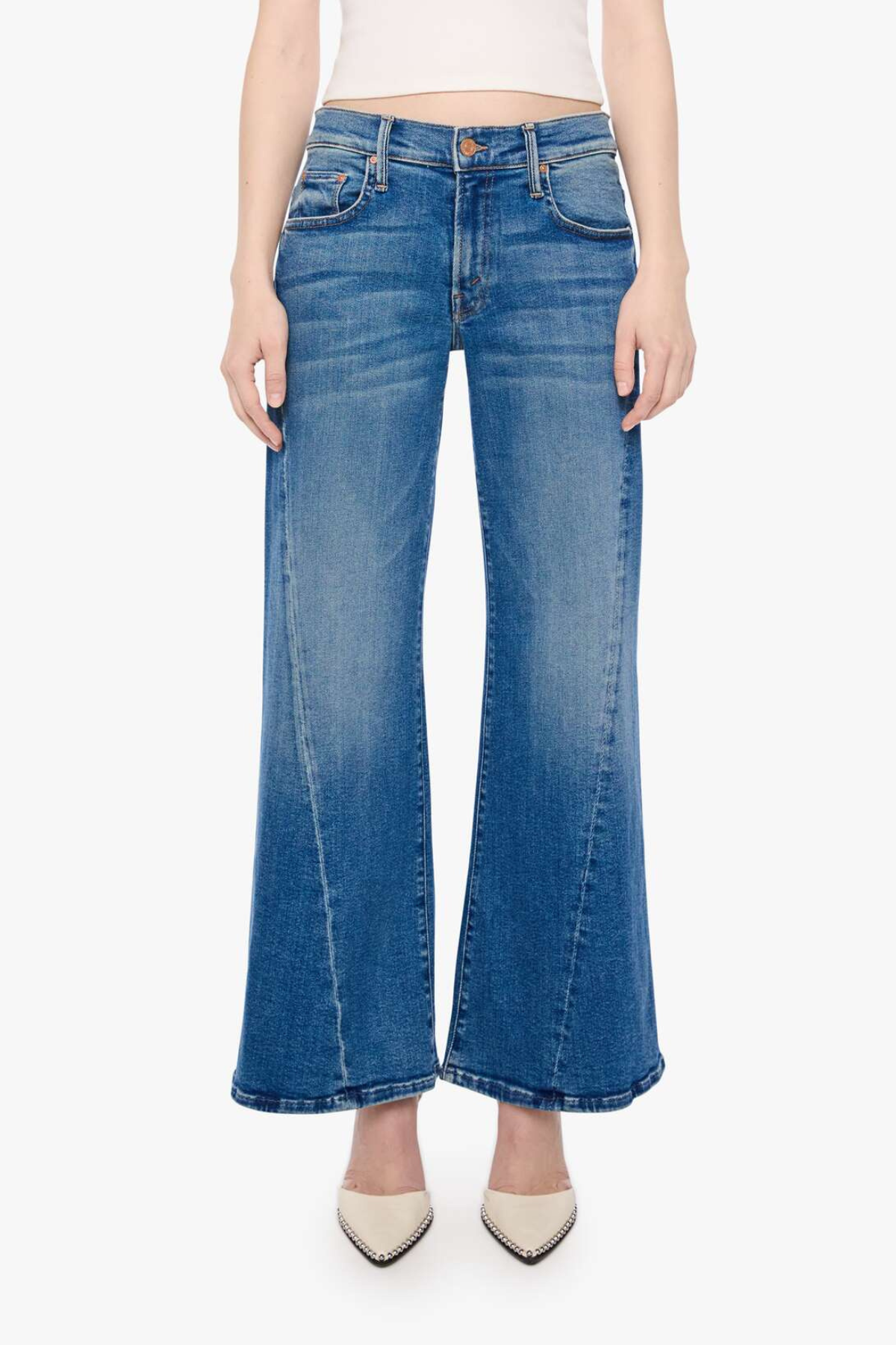 A model wearing a pair of medium-wash blue denim flare jeans with a straight-to-wide leg, paired with beige pointed-toe heels against a plain white background.
