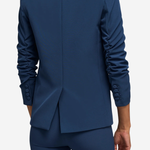 A person shown from the back wearing a tailored navy blue blazer and matching trousers against a light gray studio background.