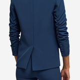 A person shown from the back wearing a tailored navy blue blazer and matching trousers against a light gray studio background.