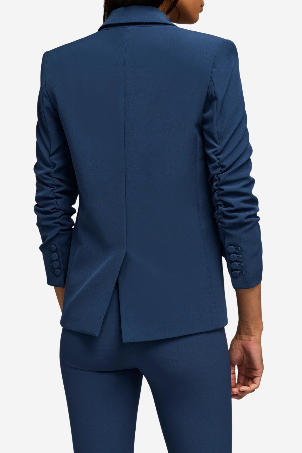 A person shown from the back wearing a tailored navy blue blazer and matching trousers against a light gray studio background.