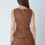 A woman shown from the back wearing a sleeveless brown faux-leather top with a gold-tone zipper and a matching brown pleated skirt, against a light gray studio background.
