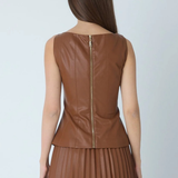 A woman shown from the back wearing a sleeveless brown faux-leather top with a gold-tone zipper and a matching brown pleated skirt, against a light gray studio background.