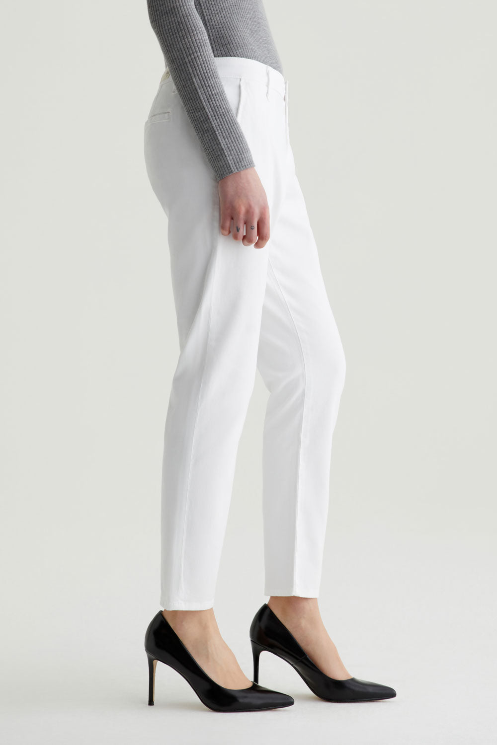 Person wearing white pants and black high heels on a plain background
