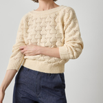 Woman wearing a cream knitted sweater and dark blue jeans on a light gray background