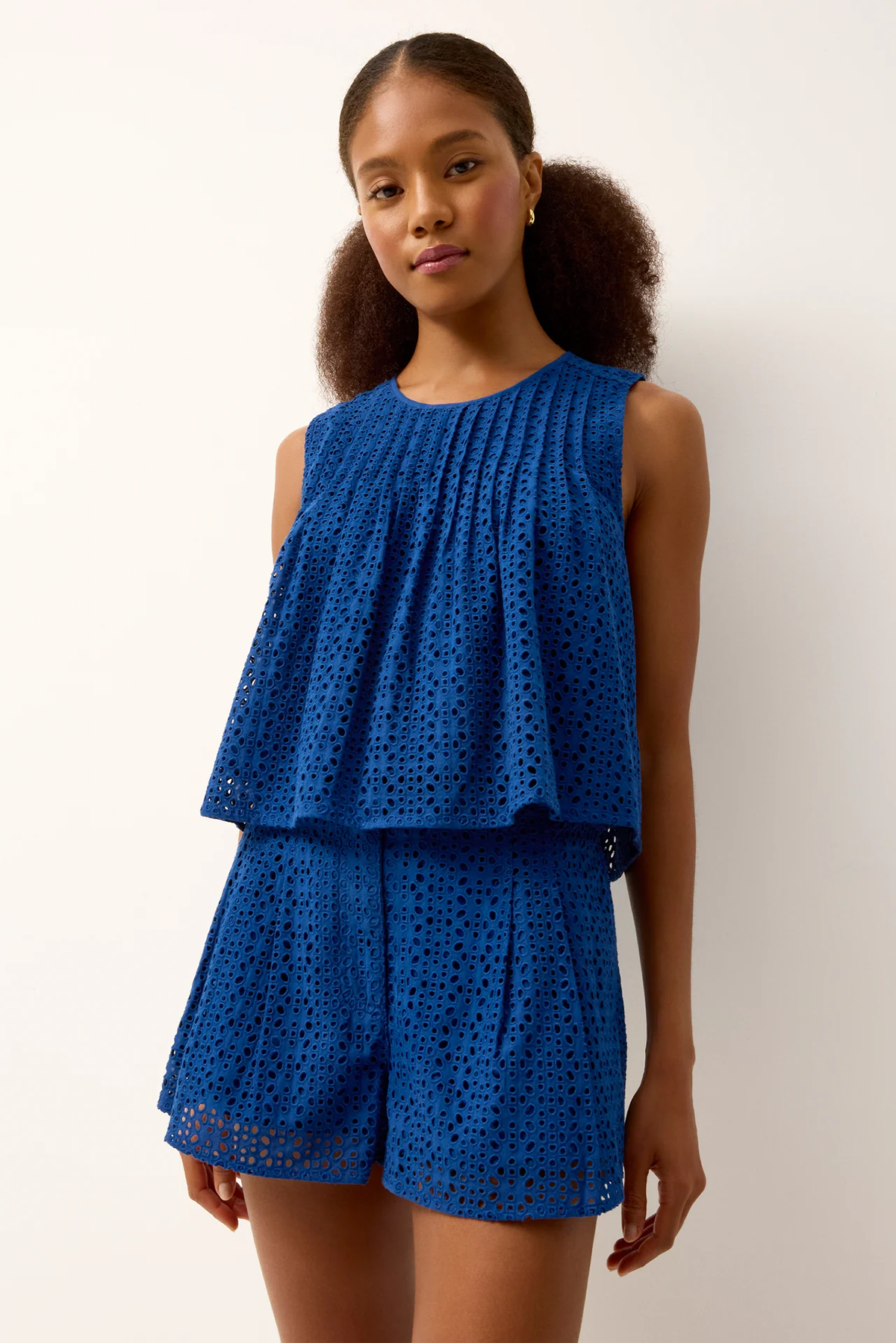 Woman wearing a blue lace top and shorts set against a white background