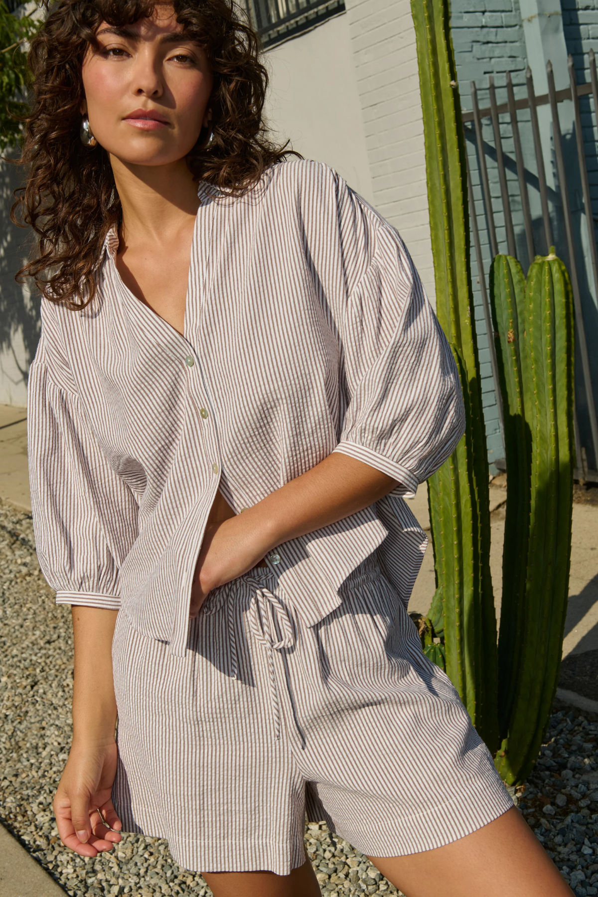 Woman wearing a striped shirt and shorts standing outdoors with a cactus in the background