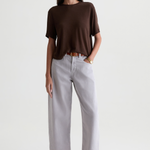 A woman modeling a dark brown short-sleeve knit top and light gray wide-leg cropped pants with brown leather loafers, shot against a plain light gray studio background.