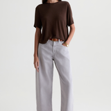 A woman modeling a dark brown short-sleeve knit top and light gray wide-leg cropped pants with brown leather loafers, shot against a plain light gray studio background.