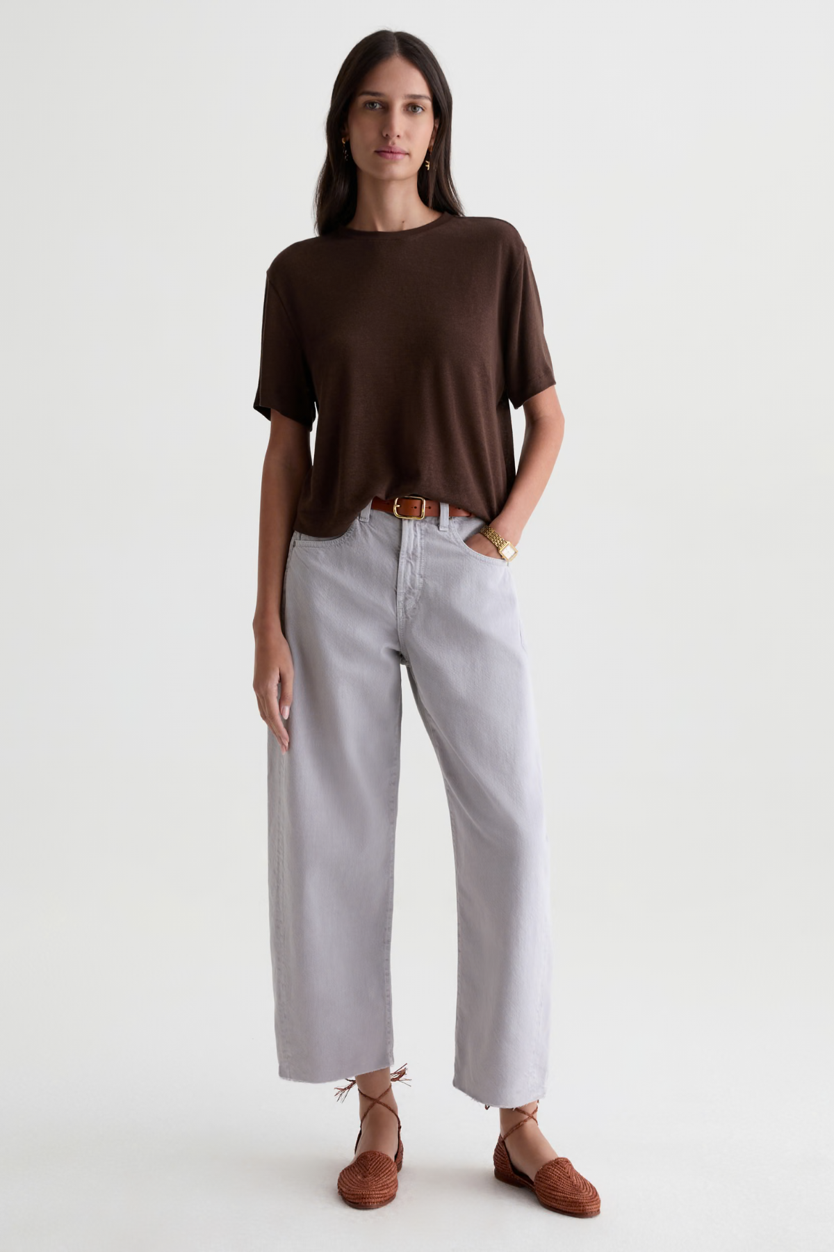 A woman modeling a dark brown short-sleeve knit top and light gray wide-leg cropped pants with brown leather loafers, shot against a plain light gray studio background.