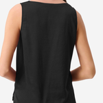 A woman shown from the back wearing a sleeveless black top and black pants against a light gray studio background.