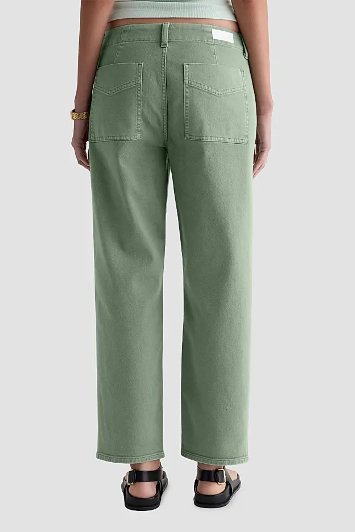 A person shown from the back wearing sage green wide-leg cropped jeans with black sandals, against a light gray studio background.