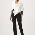 A model wearing a cream-colored wrap shawl with a fluffy pom-pom detail at the center, styled over a black top against a light gray studio background.