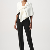 A model wearing a cream-colored wrap shawl with a fluffy pom-pom detail at the center, styled over a black top against a light gray studio background.
