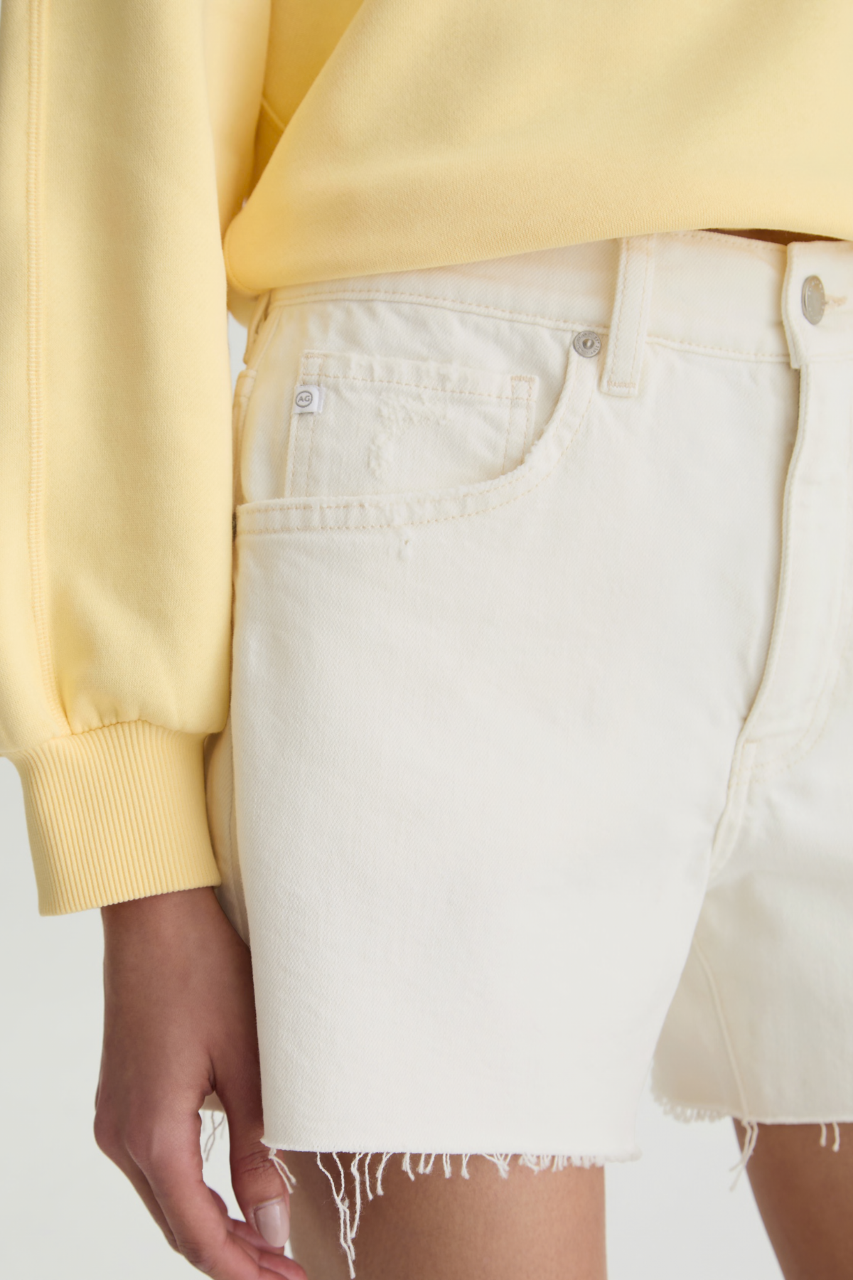 Person wearing a yellow sweater and white denim shorts on a light gray background
