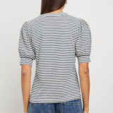 Person wearing a black and white striped shirt and blue jeans on a plain background