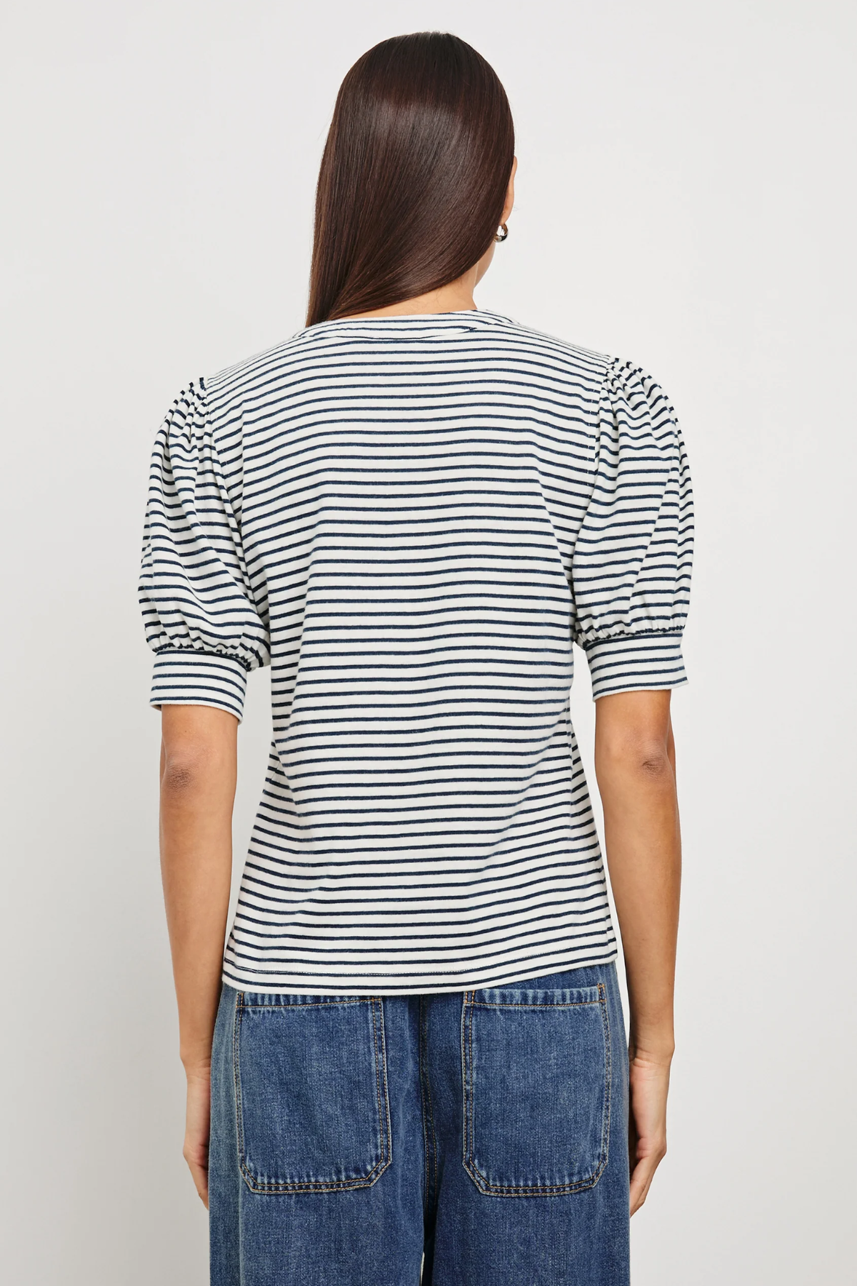 Person wearing a black and white striped shirt and blue jeans on a plain background