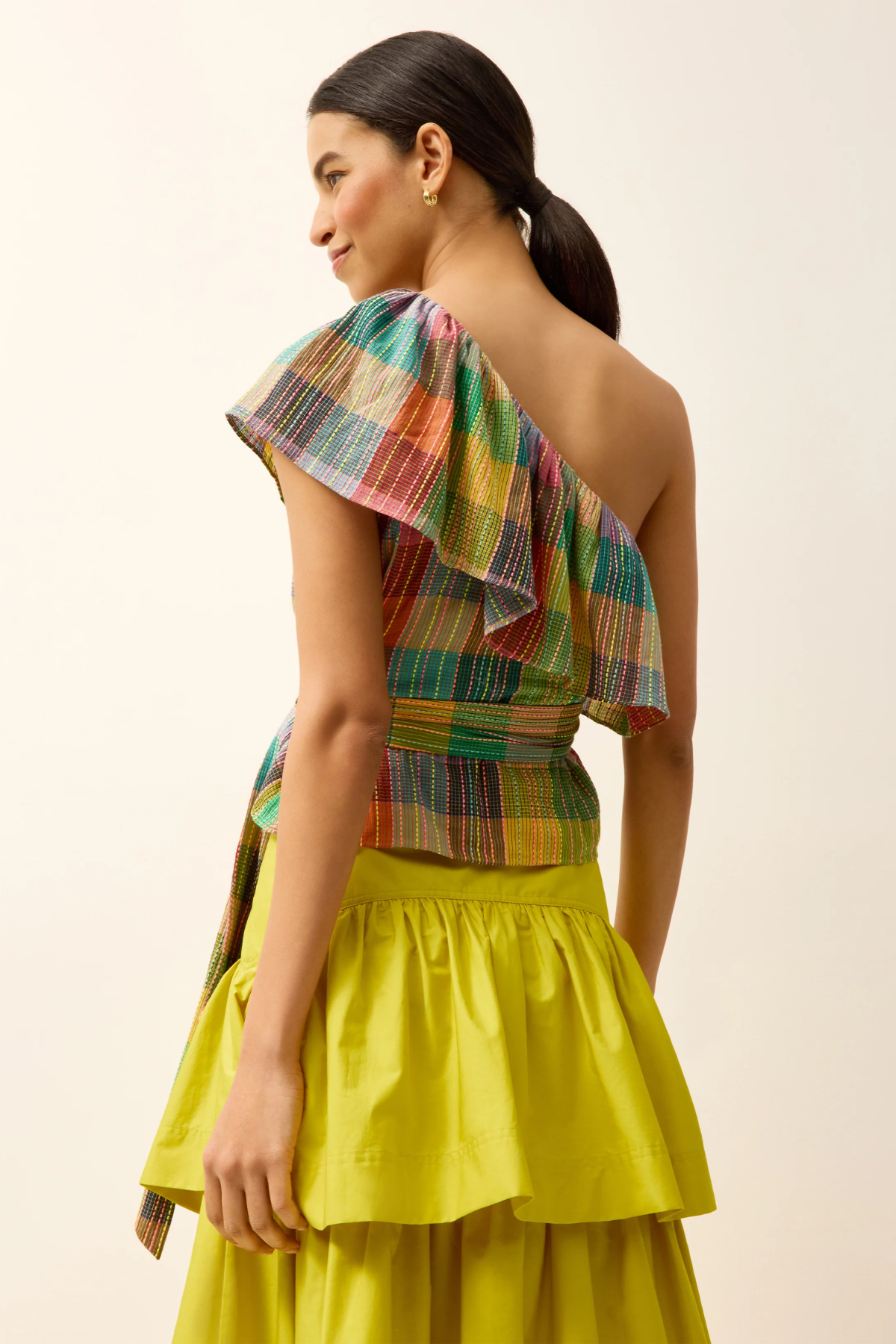 Woman wearing a colorful one-shoulder top and yellow skirt against a plain background