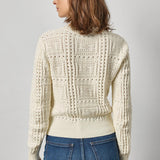 Woman wearing a cream knitted sweater and blue jeans on a gray background