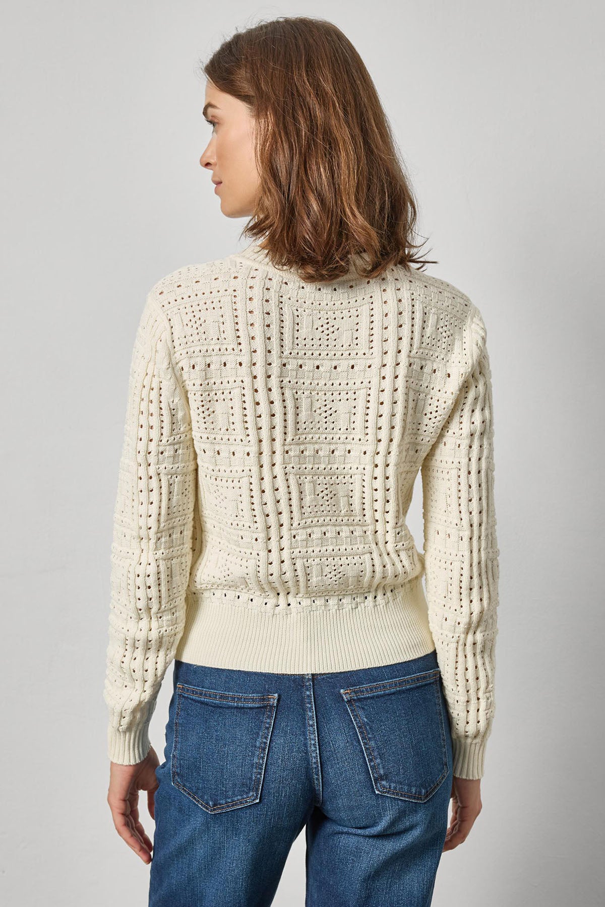 Woman wearing a cream knitted sweater and blue jeans on a gray background