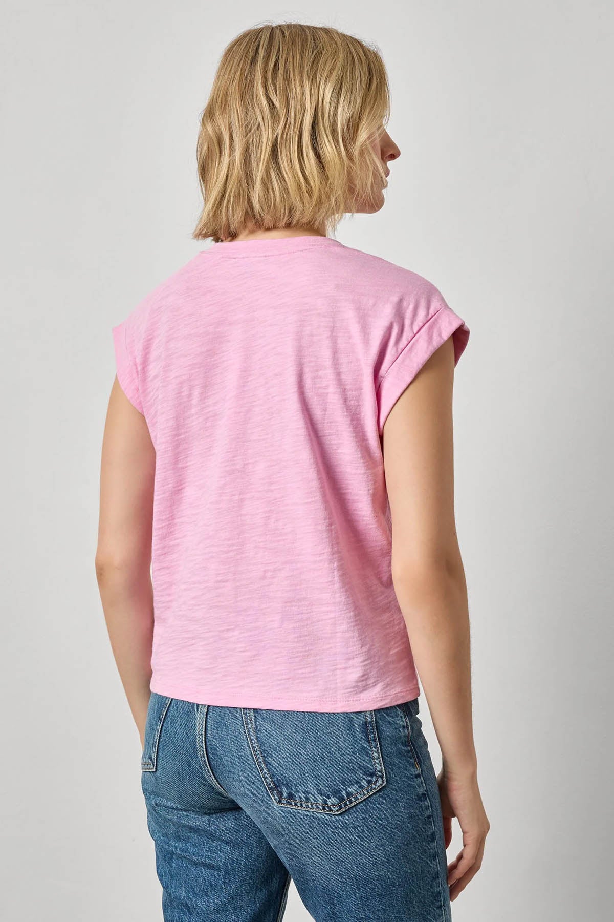 Person wearing a pink sleeveless top and blue jeans on a plain background