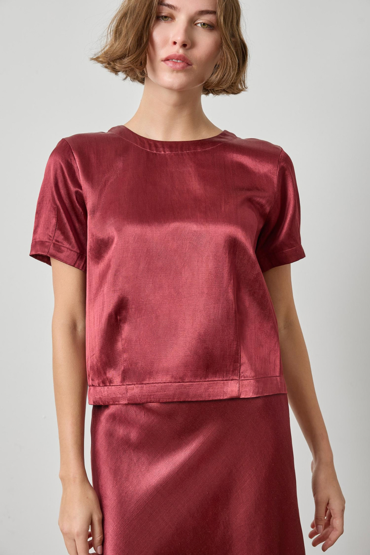 Woman wearing a red satin top and skirt on a plain background