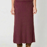 A model wearing a ribbed knit midi skirt in a deep plum purple color, paired with brown suede ankle boots, shown from the waist down against a light gray background.