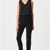 A woman modeling a black sleeveless top with a scalloped V-neckline and black cropped pants, paired with pointed-toe heeled sandals, against a plain light gray studio background.