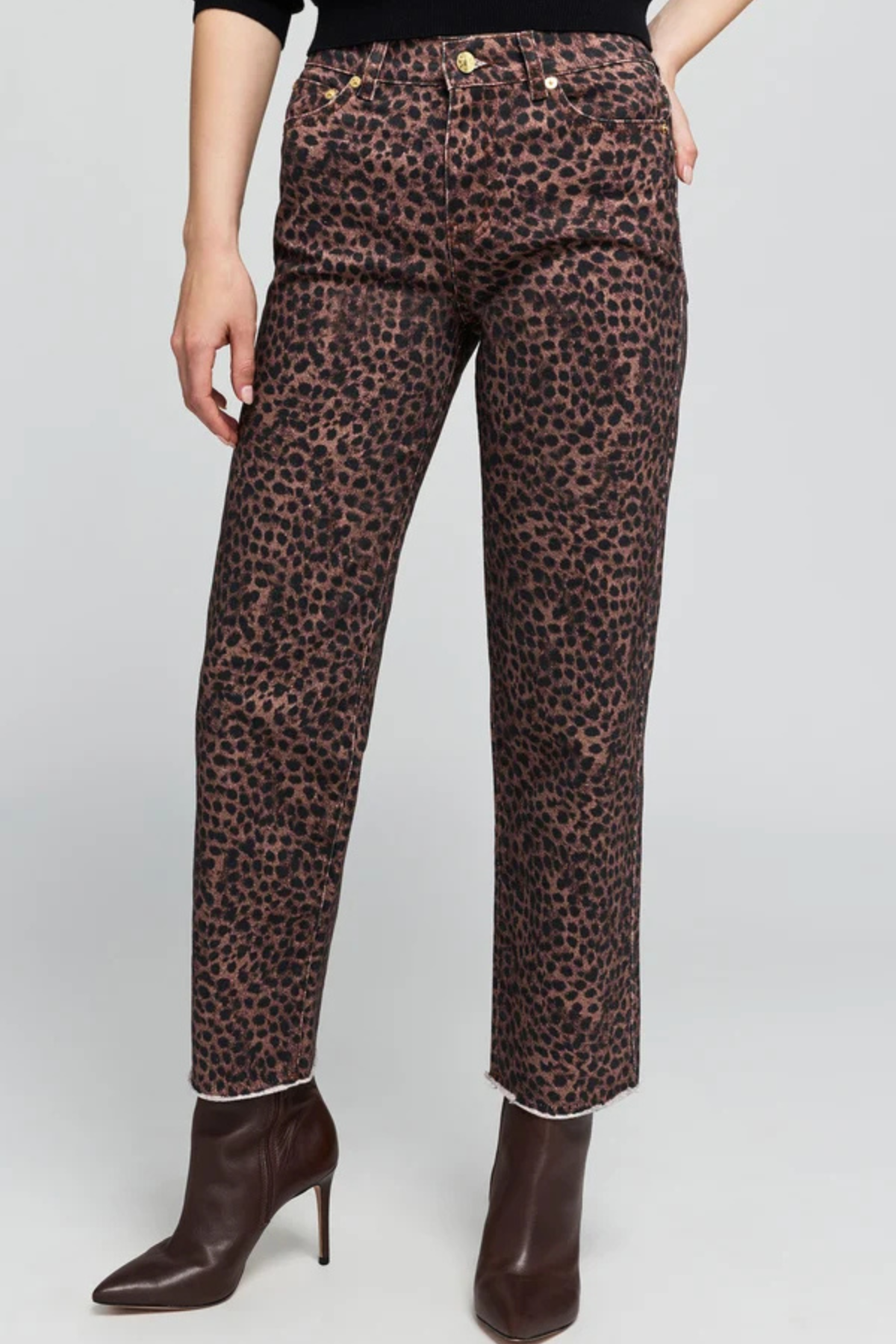 A model wearing leopard print cropped jeans with a brown and black animal pattern, paired with dark brown pointed-toe ankle boots, shown against a light gray studio background.