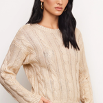 A woman modeling a cream cable-knit crewneck sweater against a plain light background.