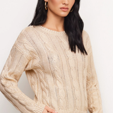 A woman modeling a cream cable-knit crewneck sweater against a plain light background.