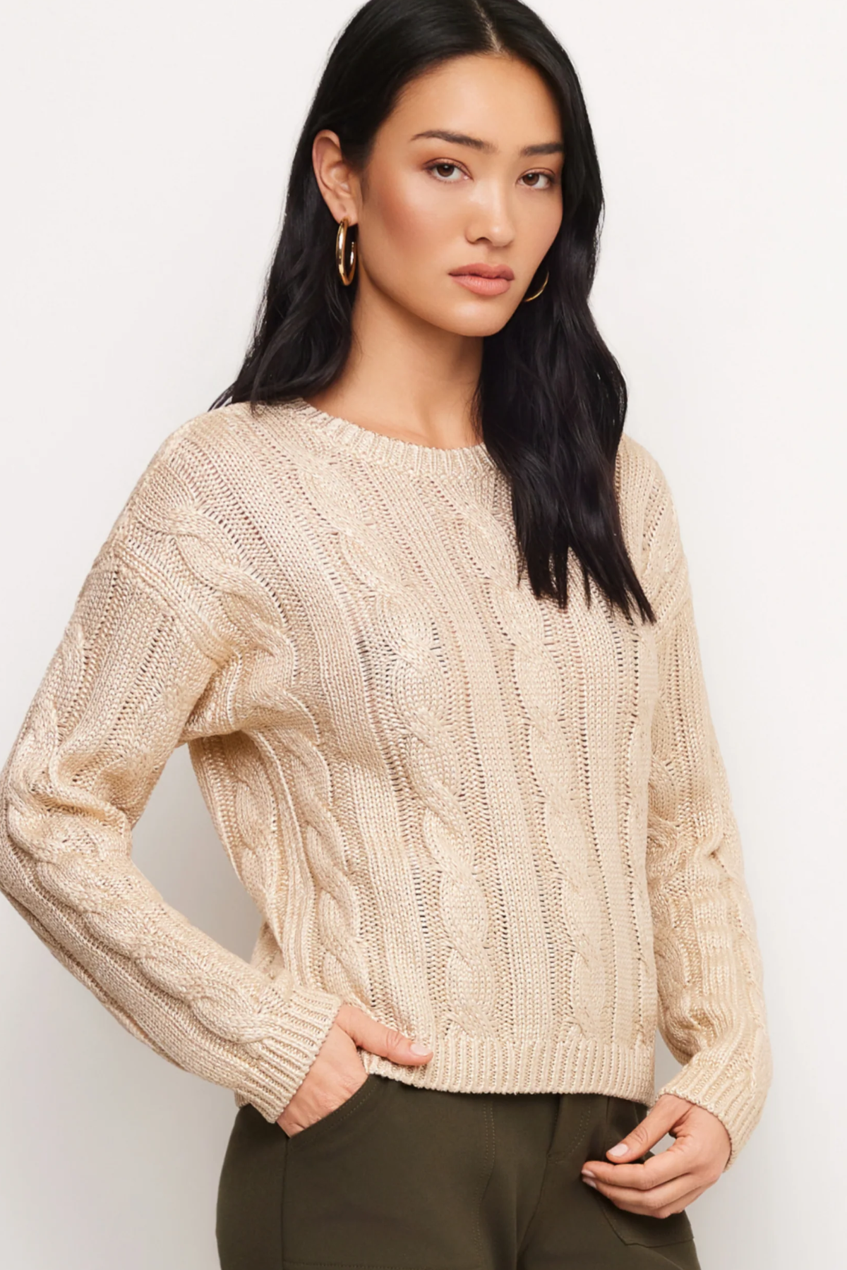 A woman modeling a cream cable-knit crewneck sweater against a plain light background.