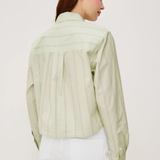 Woman wearing a light green shirt and white pants on a plain background