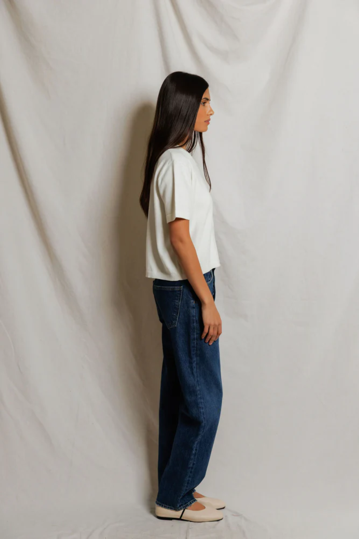 Woman wearing a white t-shirt and blue jeans standing against a plain white background