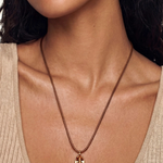 A close-up of a model wearing a delicate brown chain necklace with a small gold anchor pendant, paired with a beige ribbed scoop-neck top.