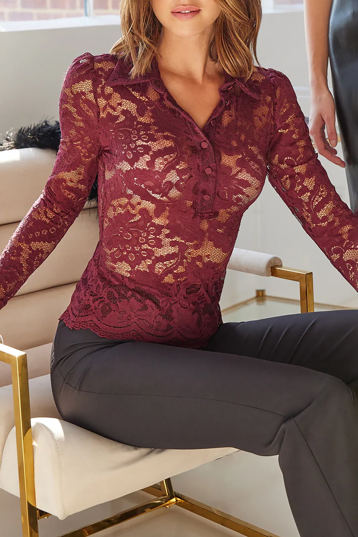 Woman wearing a red lace top sitting on a chair indoors.