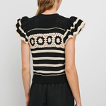 Woman wearing a black and white patterned top with ruffled sleeves on a plain background