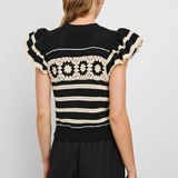 Woman wearing a black and white patterned top with ruffled sleeves on a plain background