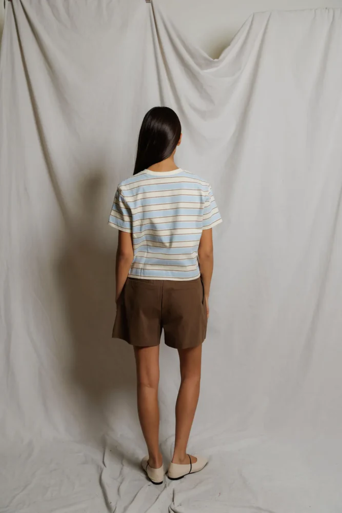 Person wearing a striped shirt and brown shorts standing against a plain white backdrop