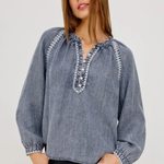 Woman wearing a blue denim blouse with intricate detailing on a plain background