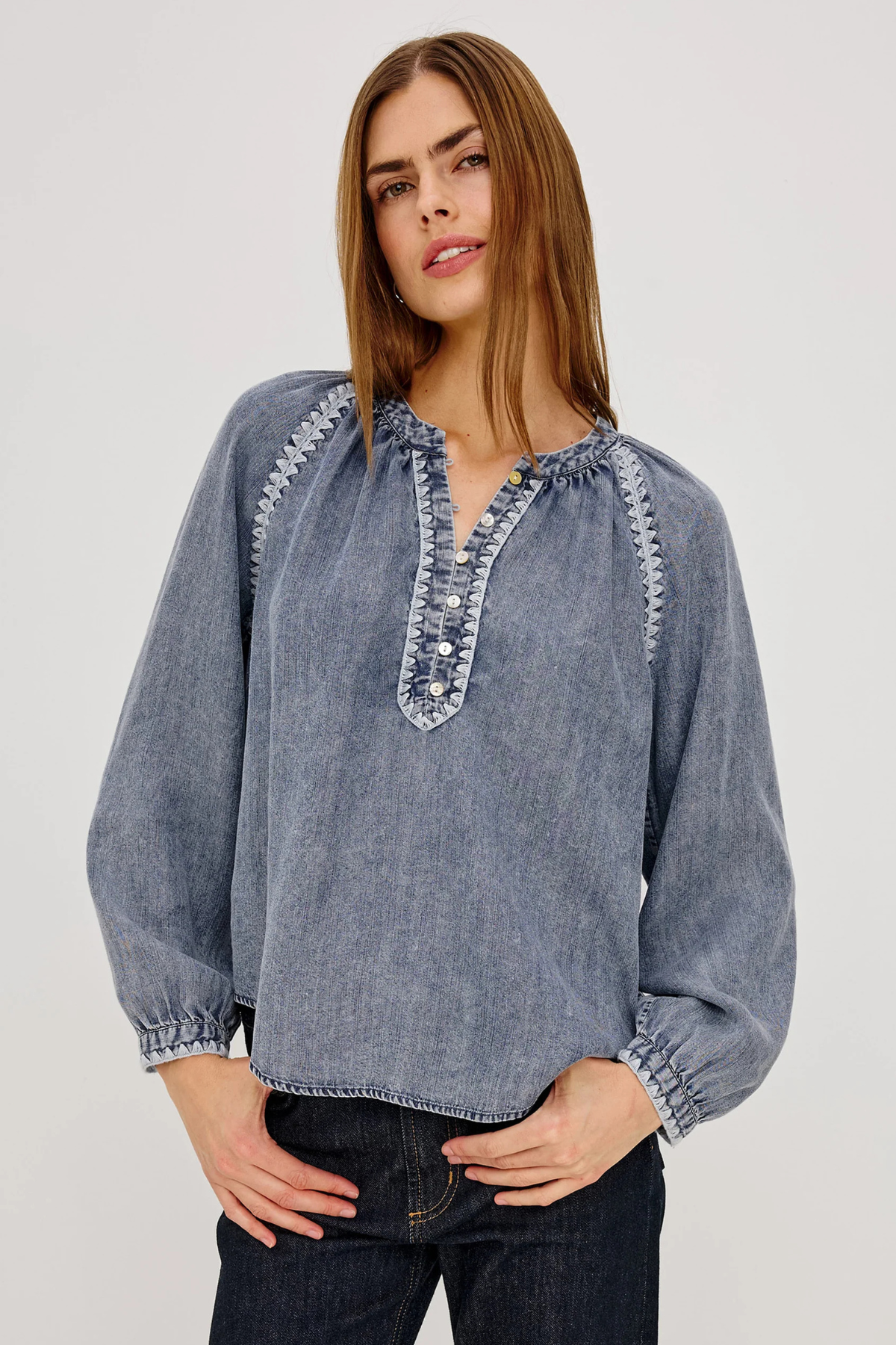 Woman wearing a blue denim blouse with intricate detailing on a plain background