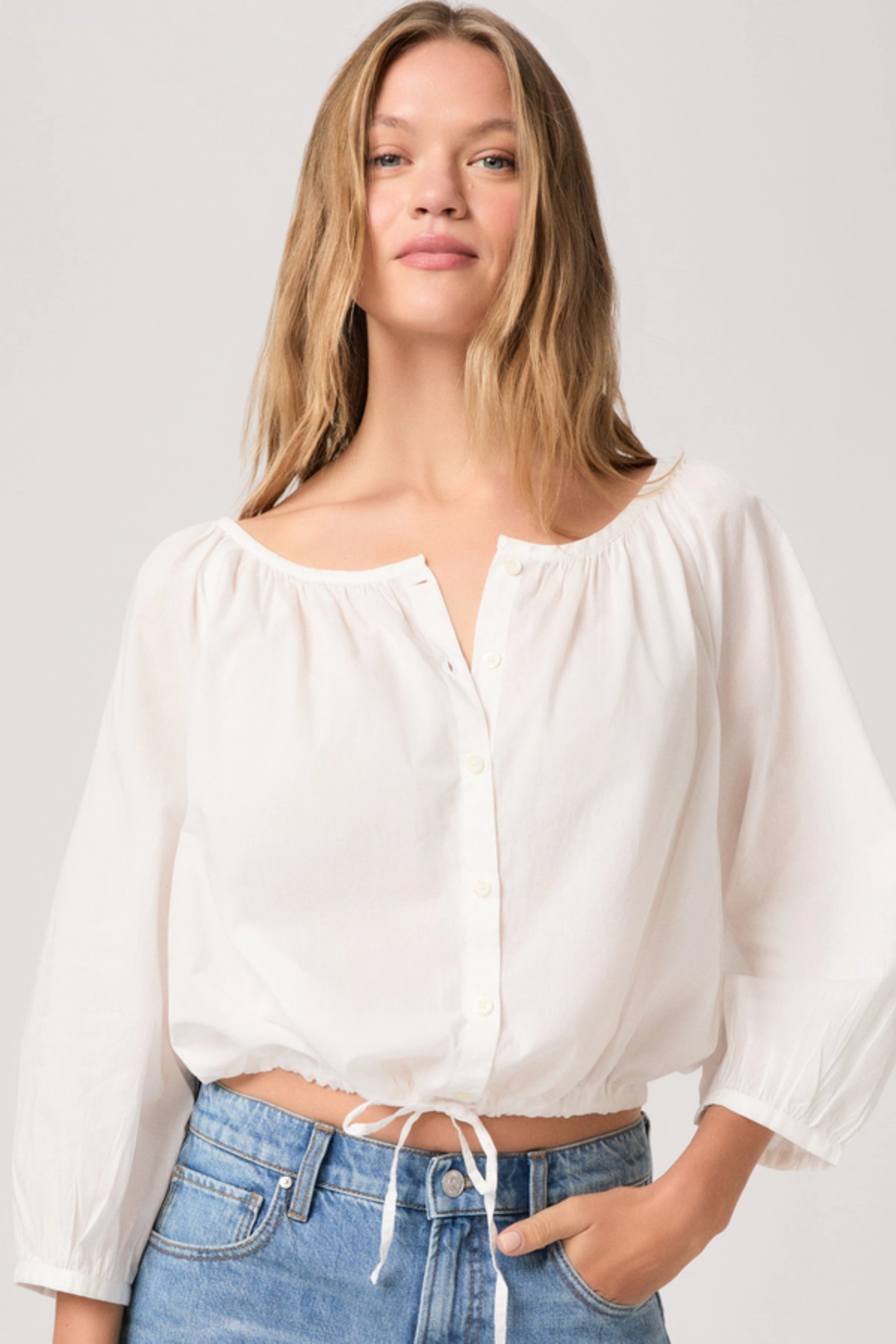 Woman wearing a white blouse and blue jeans against a plain background