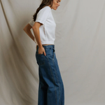 side view of woman in white top and denim on draped background 